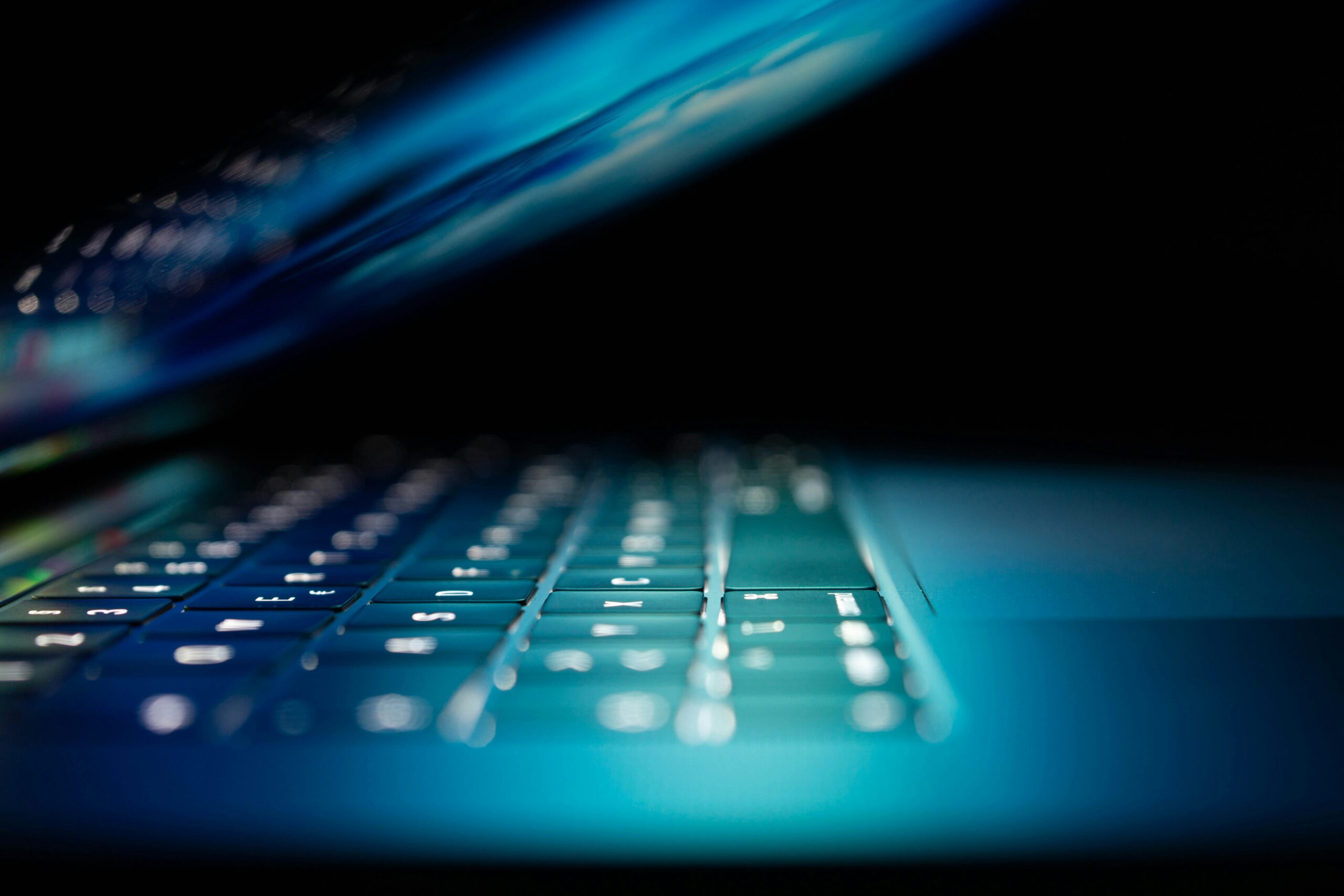 Closeup photo of a turned on laptop. Blue keys, dark background.