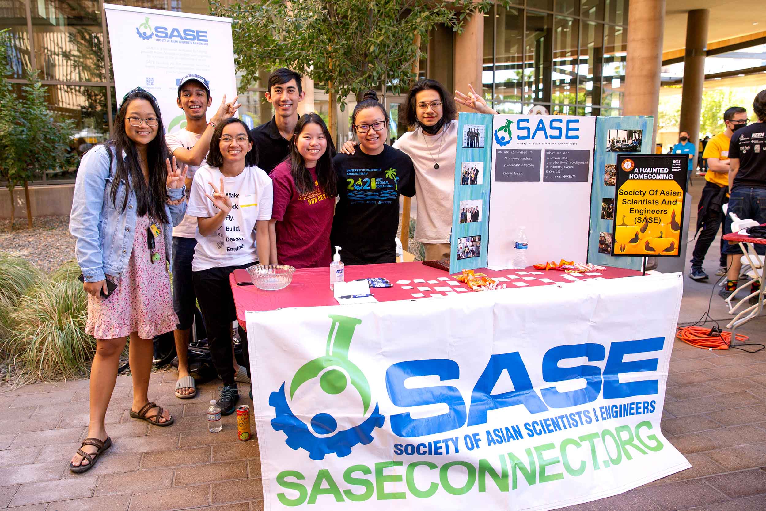 A group of Society of Asian Scientists & Engineers (SASE) members group together for a photo at their Block Party table.