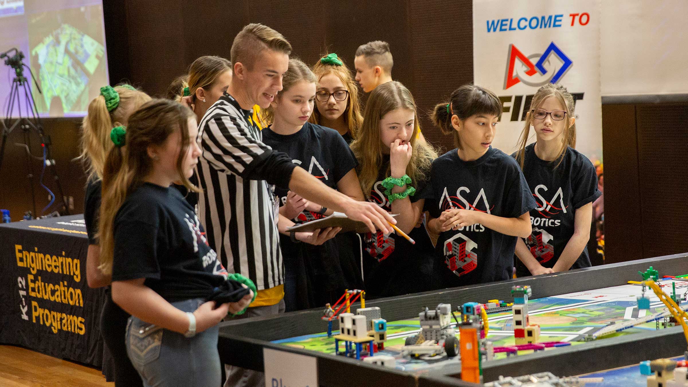 An ASU student volunteers as a judge at the FIRST LEGO League state championship. He discusses a project with the all-girls team.