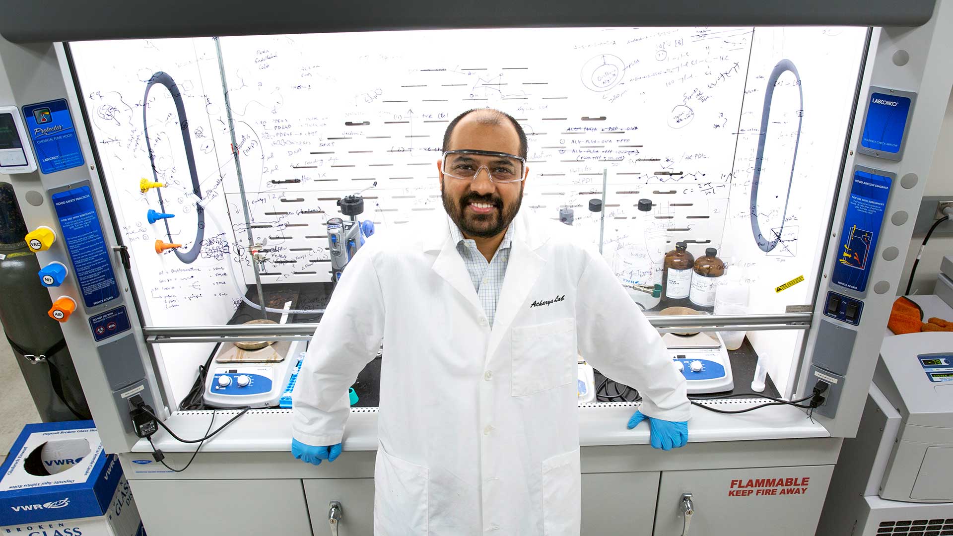 Portrait of Abhinav Acharya standing in front of a fume hood in his lab