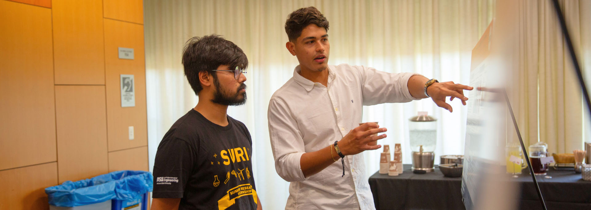 Two SURI students talk together in front of a white board.